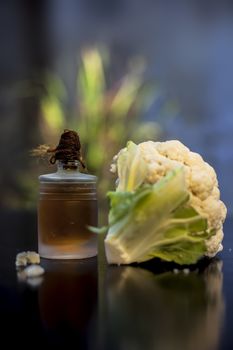 Close up shot of raw cauliflower and its essential oil in a small glass bottle on a black surface with selective focus, creative lighting, and blurred background.