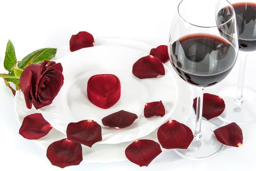 Table setting for a romantic Valentines Day dinner with a red rose, red wine and gift.