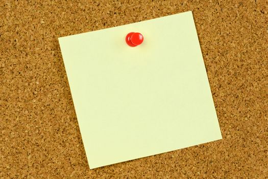 Blank yellow sticky note held on a cork notice board with a red pushpin.
