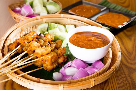 Chicken sate with delicious peanut sauce, ketupat, onion and cucumber on wooden dining table, one of famous local malaysia dishes.