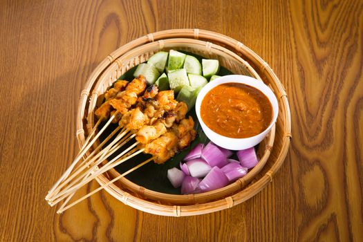 Chicken sate with delicious peanut sauce, ketupat, onion and cucumber on wooden dining table, one of famous local malaysia dishes.