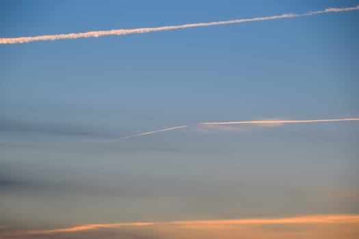 Contrail from an airplane on a blue sky against a sunset.