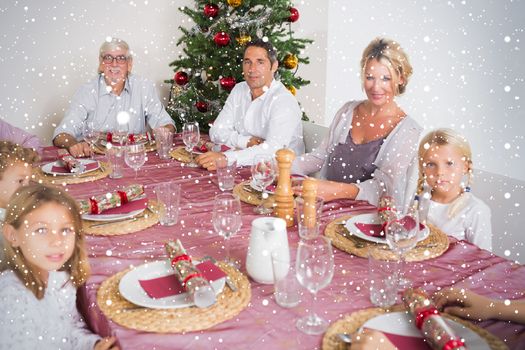 Composite image of Smiling family at the dinner table against snow falling