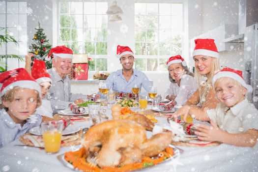 Composite image of Smiling family around the dinner table at christmas against snow