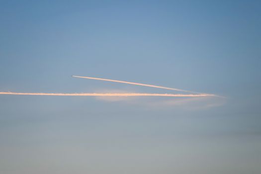 Contrail from an airplane on a blue sky against a sunset.