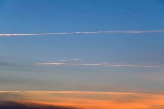 Contrail from an airplane on a blue sky against a sunset.