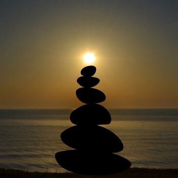 Zen concept with pyramid of stones on the beach and sun in top of it