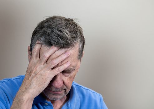 Head and shoulders portrait of a senior caucasian man with head in hands and looking depressed