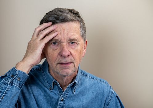 Head and shoulders portrait of a senior caucasian man with head in hands and looking depressed