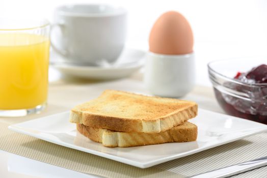 Crispy toast on a plate and a soft-boiled egg next to orange juice , cup of coffee and raspberry jam on a white background.