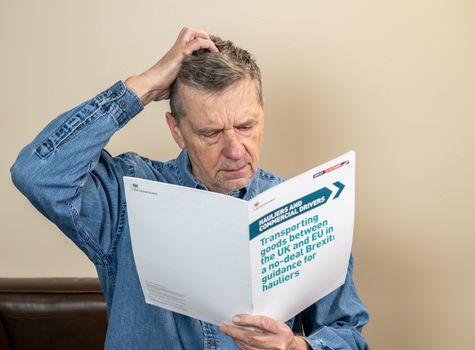 Worried senior man reading rules for transporting good to Europe in the event of no deal Brexit