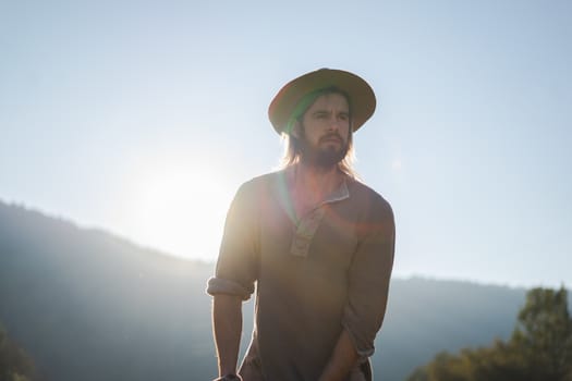 Young man with a beard and a hat on a beautiful sunset in the mountains