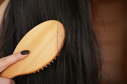 Female hand holds a black wig with long hair and combs a wooden comb. Hairdresser and hair care