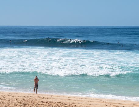 Many surfers waiting for big wave in the sea at Banzai Pipeline on north coast of Oahu, Hawaii