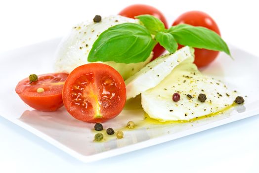 Delicacy of Italian cuisine - mozzarella cheese with basil leaves and baby tomatoes, flavored with olive oil and pepper