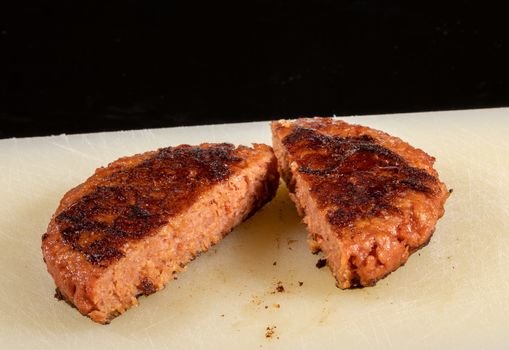 Charred and ready to eat plant-based burger in cut in half on cutting board