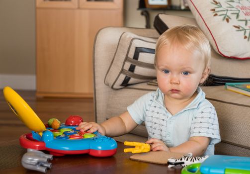 Baby boy sitting on the floor of living room and playing with toy computer and animals