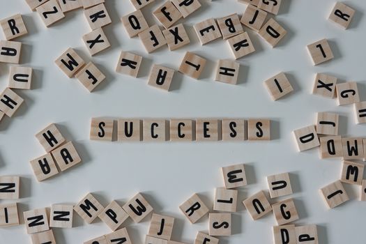 Success written in wooden letter tiles surrounded by random letters on a white background