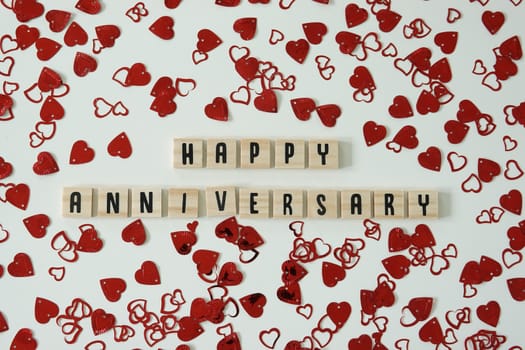 Happy anniversary written in wooden letter tiles with heart shaped confetti surrounding it.