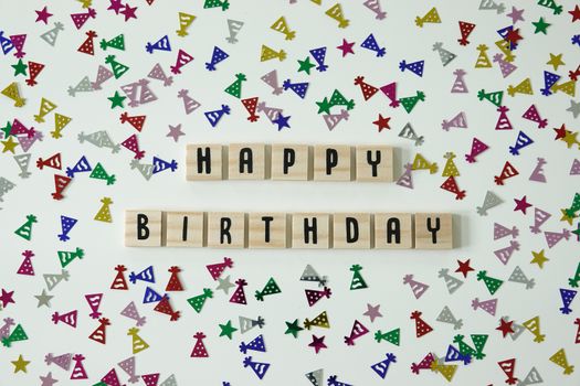 Happy birthday written in wooden letter tiles with confetti birthday hats and stars surrounding it.