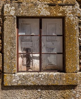 Broken glass pane and wooden shutters in stone window and wall of old house in the ancient town of Castelo Rodrigo in Portugal
