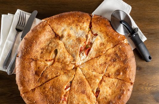 Layflat from above large double crust pizza with slicing tool and cutlery and white cotton napkins