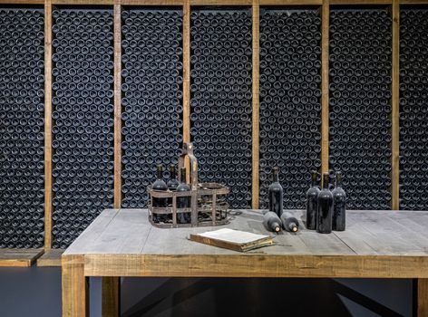 Stacks of wine bottles laying flat in wooden racks in old wine cellar or cave with tasting table