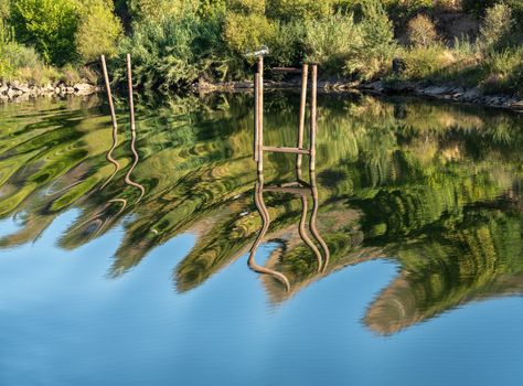 Wavy stakes and wooden poles for boat moorings and anchors reflected in calm Douro river in Portugal