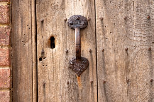 Ancient exterior door in worn and weathered wood with rusty handle and key hole for lock