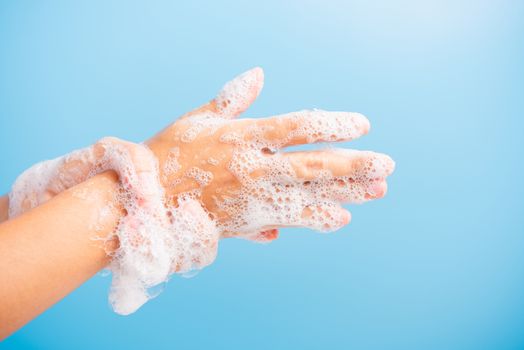 Closeup body care Asian young woman washing hands with soap have foam, hygiene prevention COVID-19 or coronavirus protection concept, isolated on blue background