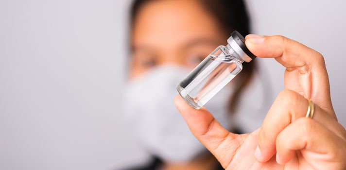 Asian woman doctor wearing surgical protective cloth face mask against coronavirus her hold ampoule bottle vaccine focus on  glass transparent, studio shot isolated white background, COVID-19 concept