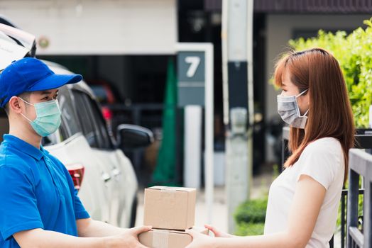 Asian young delivery man courier shopping online give package post box he protective face mask service woman customer receiving box at front home, under curfew quarantine pandemic coronavirus COVID-19