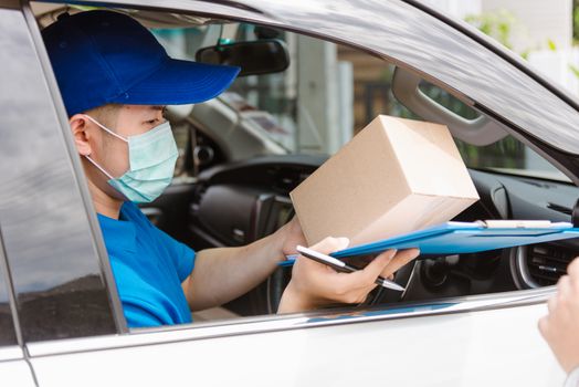 Asian delivery courier young man driver inside van car giving parcel post boxes to customer receiving both protective face mask, under curfew quarantine pandemic coronavirus COVID-19