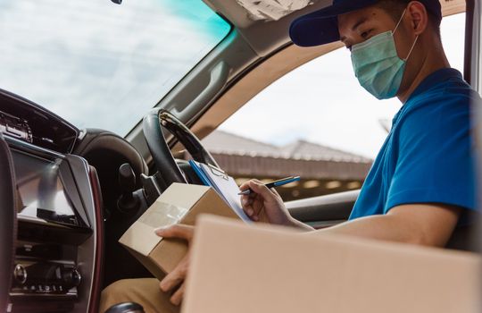 Asian delivery courier young man driver inside the van car with parcel post boxes checking amount he protective face mask, under curfew quarantine pandemic coronavirus COVID-19