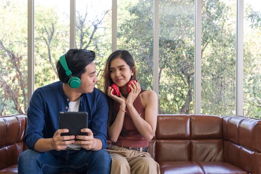 Young lovers spend time together on holidays in the living room. Both are interested in music from headphones while the man holding tablet computer.