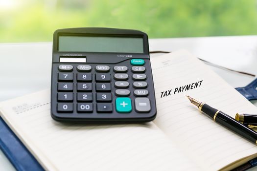 pen, calculator and notebook with TAX PAYMENT word on the white table with green backgrounds