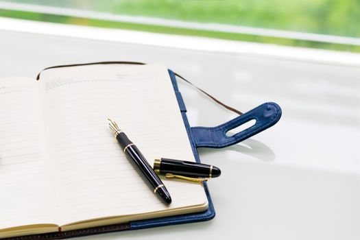 pen and notebook on the white table near window, sideview with green backgrounds