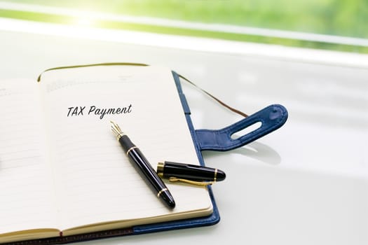 pen and notebook with TAX Payment word on the white table near window, sideview with green light backgrounds