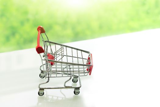 Empty shopping cart trolley on white table with green backgrounds