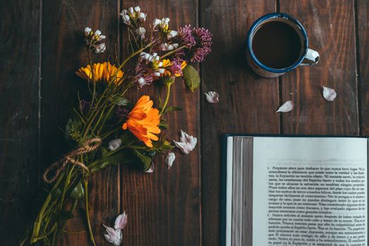 Book with spring flowers with a small white cup of coffee on a rustic wooden table