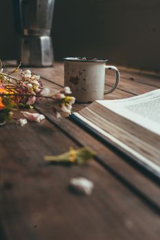 Book with spring flowers with a small white cup of coffee on a rustic wooden table
