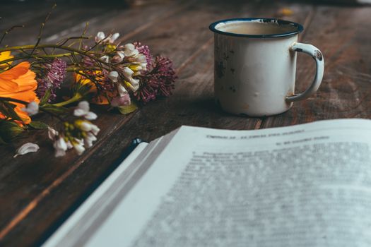 Book with spring flowers with a small white cup of coffee on a rustic wooden table