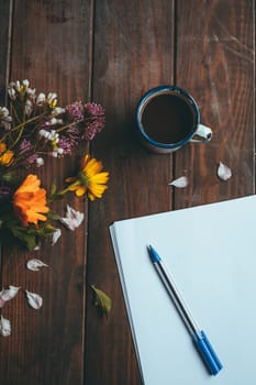 Blank paper and pen with spring flowers with a small white cup of coffee on a rustic wooden table