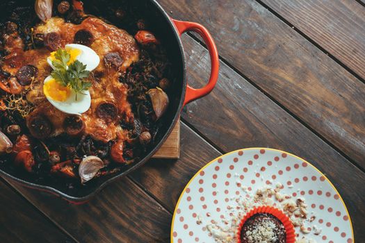 Wrought iron skillet with vegetables, meat, egg, cheese and cilantro gratin next to a plate with a chocolate cake and organic chocolate cream.