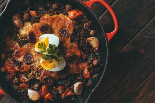 Wrought iron frying pan with vegetables, meat, egg, gratin cheese and coriander.