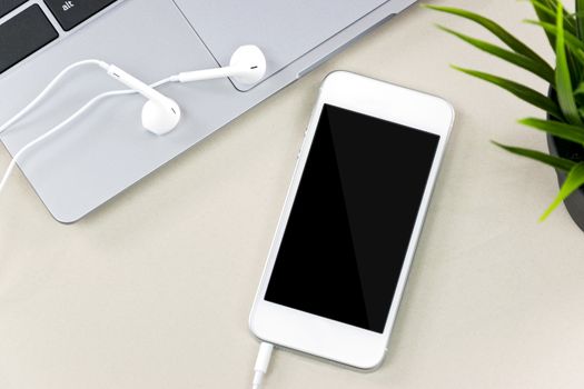 Elegant smartphone with headphones next to a laptop on a desk.