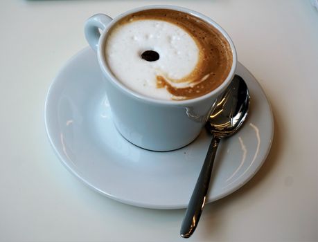 White cup of coffee with milk foam and spoon