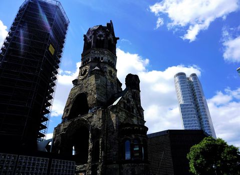 Kaier Wilhelm Memorial church and skyscraper in front of blue sky with clouds