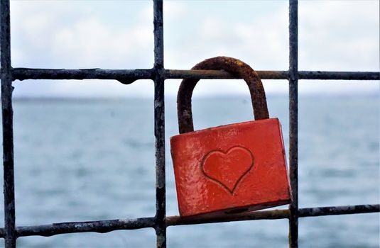 Rusty padlock with a heart and the sea in the background