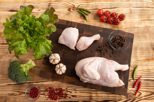 Raw chicken and vegetables for cooking lie on a wooden cutting board